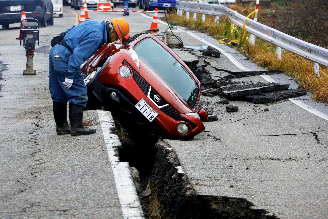 2024年1月3日，日本穴水附近，一名工人正在查看地震后困在破損道路上的汽車。